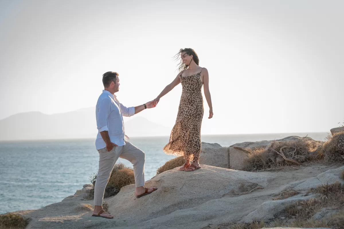 Engaged couple walking hand in hand on the rocks with a sunset backdrop in Naxos, captured by a Naxos photographer
