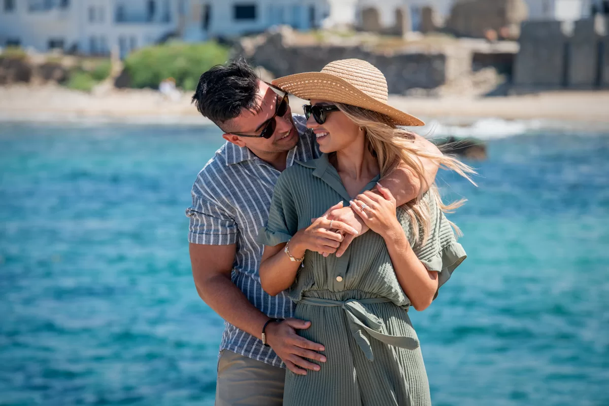 Couple wearing sunglasses pose smiling with the sea in the background, by naxos photographer