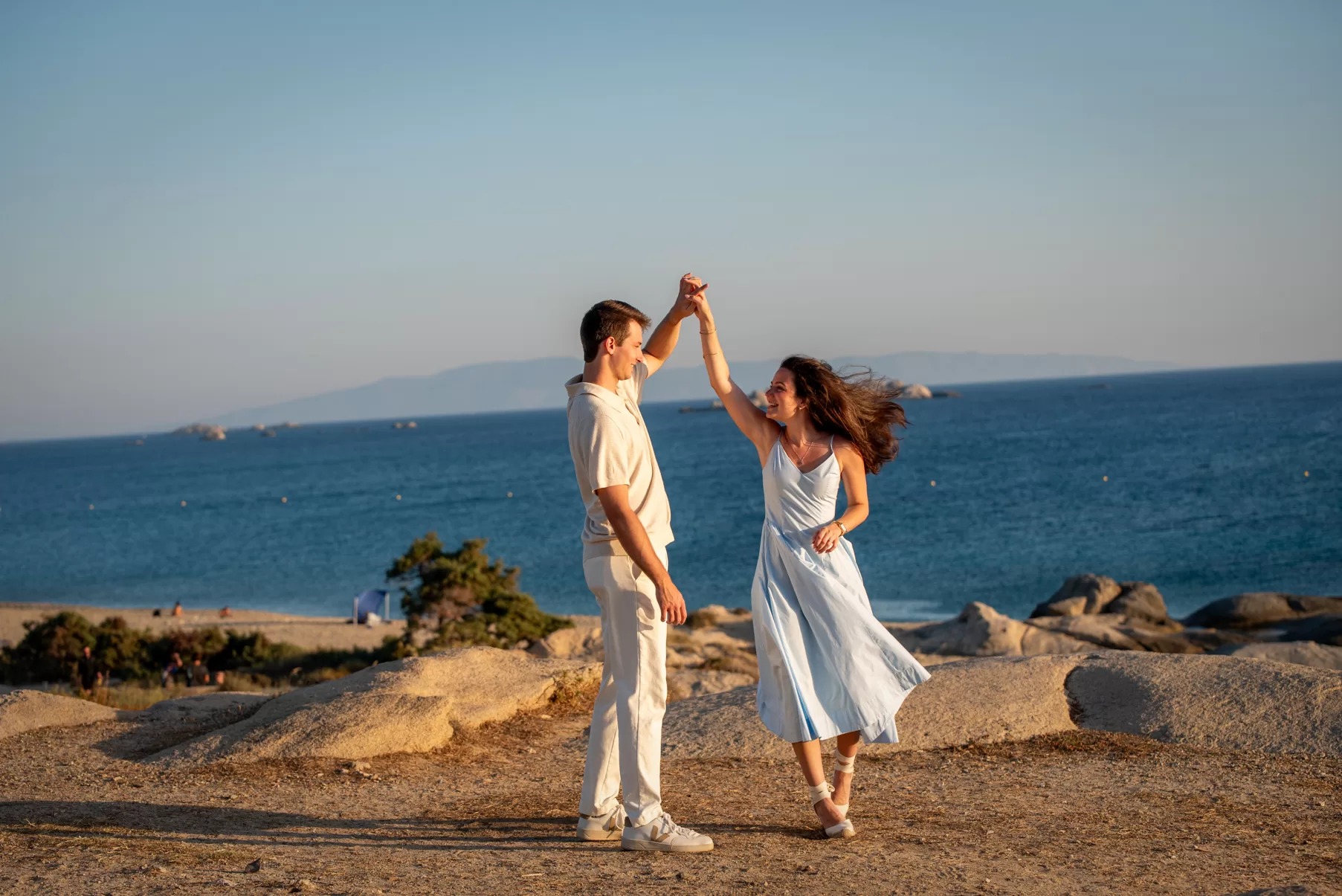 Engaged couple performing a dance move with the sea in the background, captured by naxos photographer
